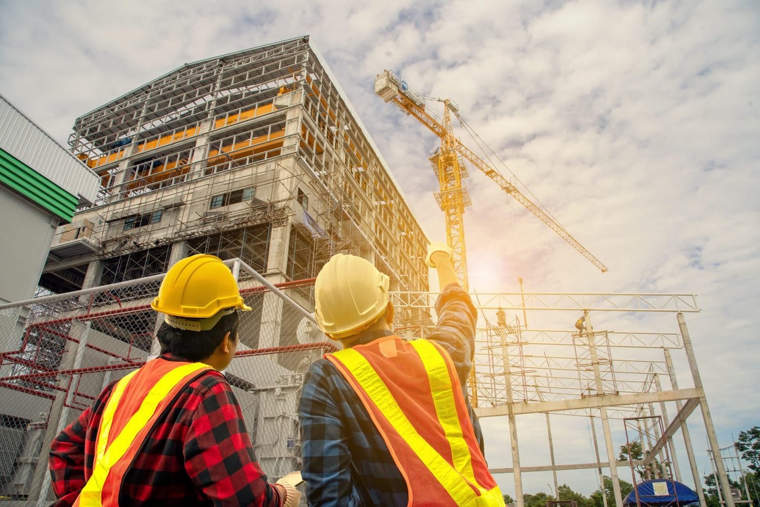 Two workers in hard hats looking up at a steel framed building and a tower crane