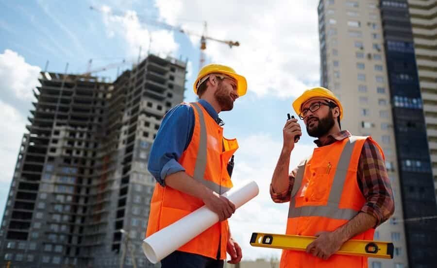 Construction crew with blueprints and a level in front of a building under construction