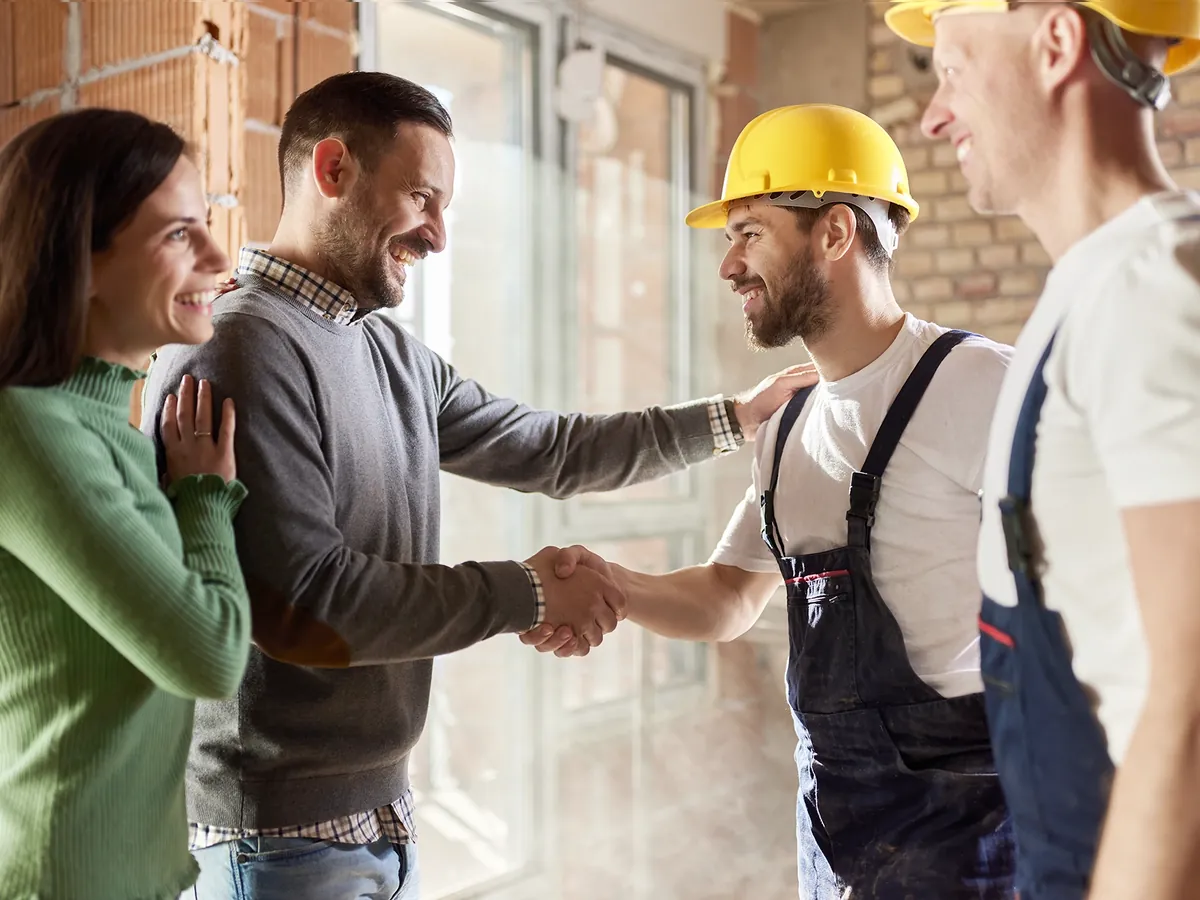 Homeowners shaking hands with contractors in hard hats inside a home under renovation