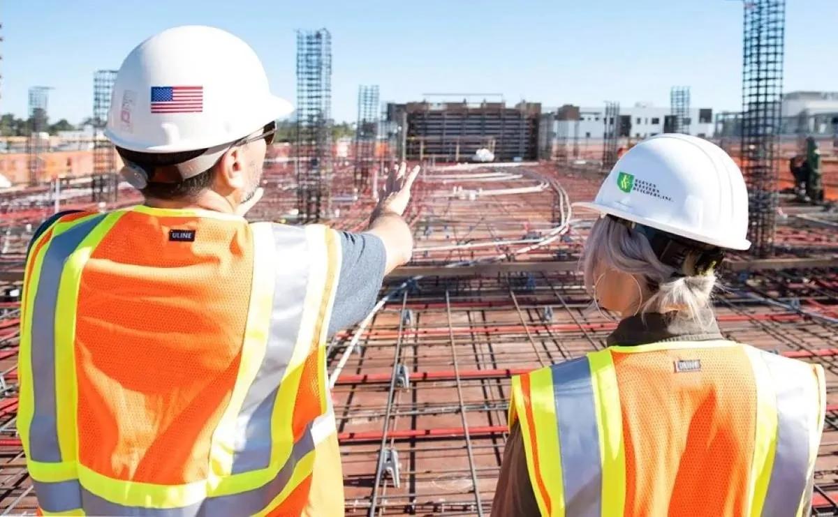 Two contractors in hard hats and safety vests reviewing a rebar foundation on a jobsite