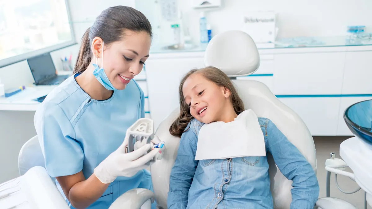 Dentist showing a young patient how to brush with a dental model