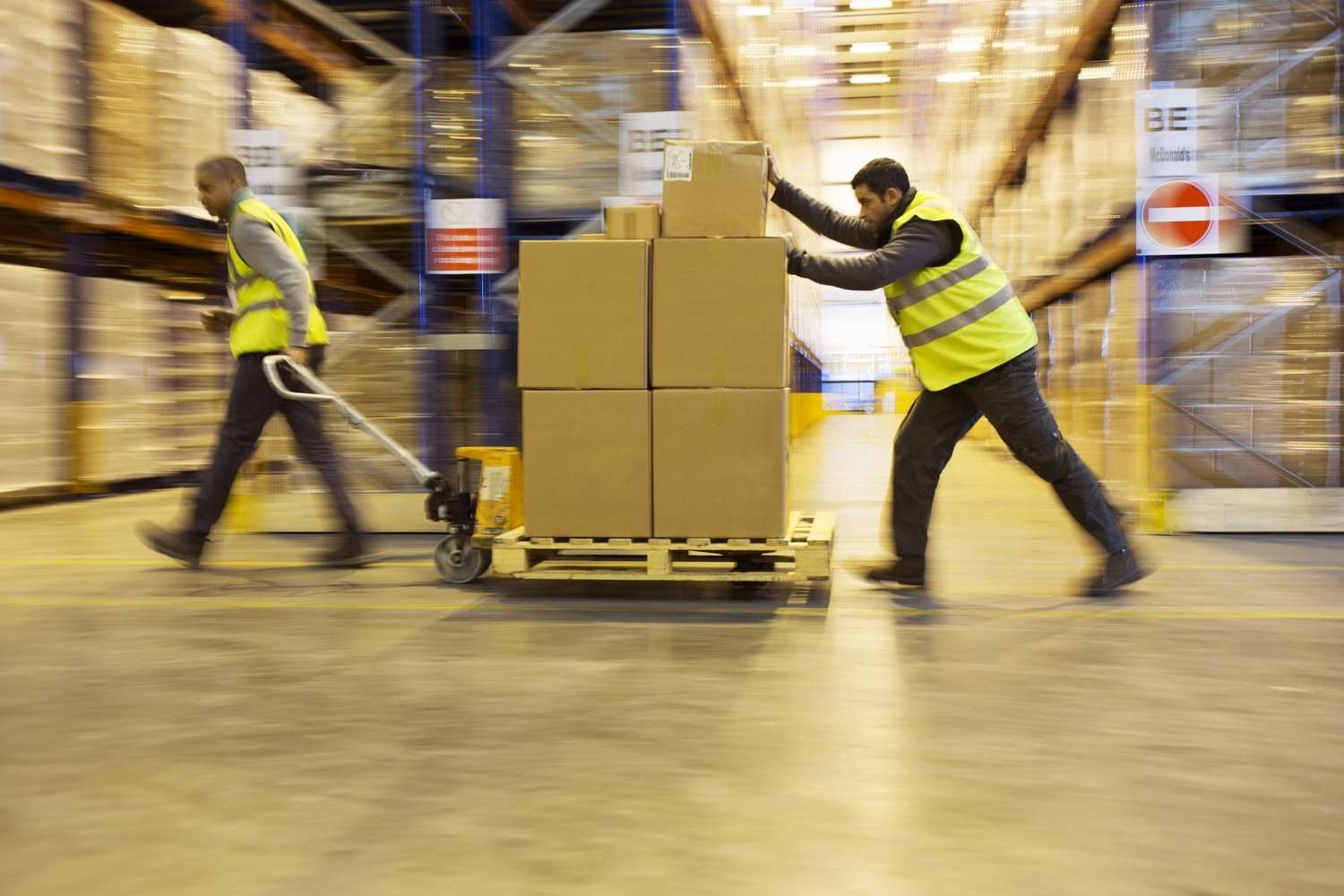 Warehouse workers moving a loaded pallet at speed down a racking aisle