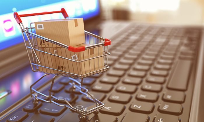 Miniature shopping cart holding a parcel on a laptop keyboard