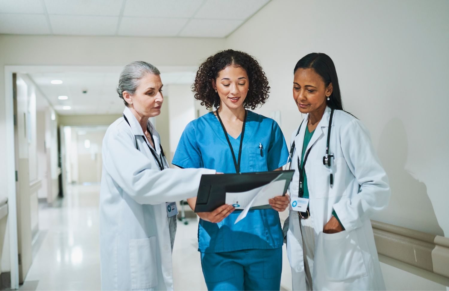 Three clinicians reviewing a patient chart together in a hospital corridor
