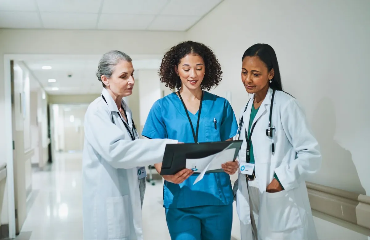 Three clinicians reviewing a patient chart together in a hospital corridor