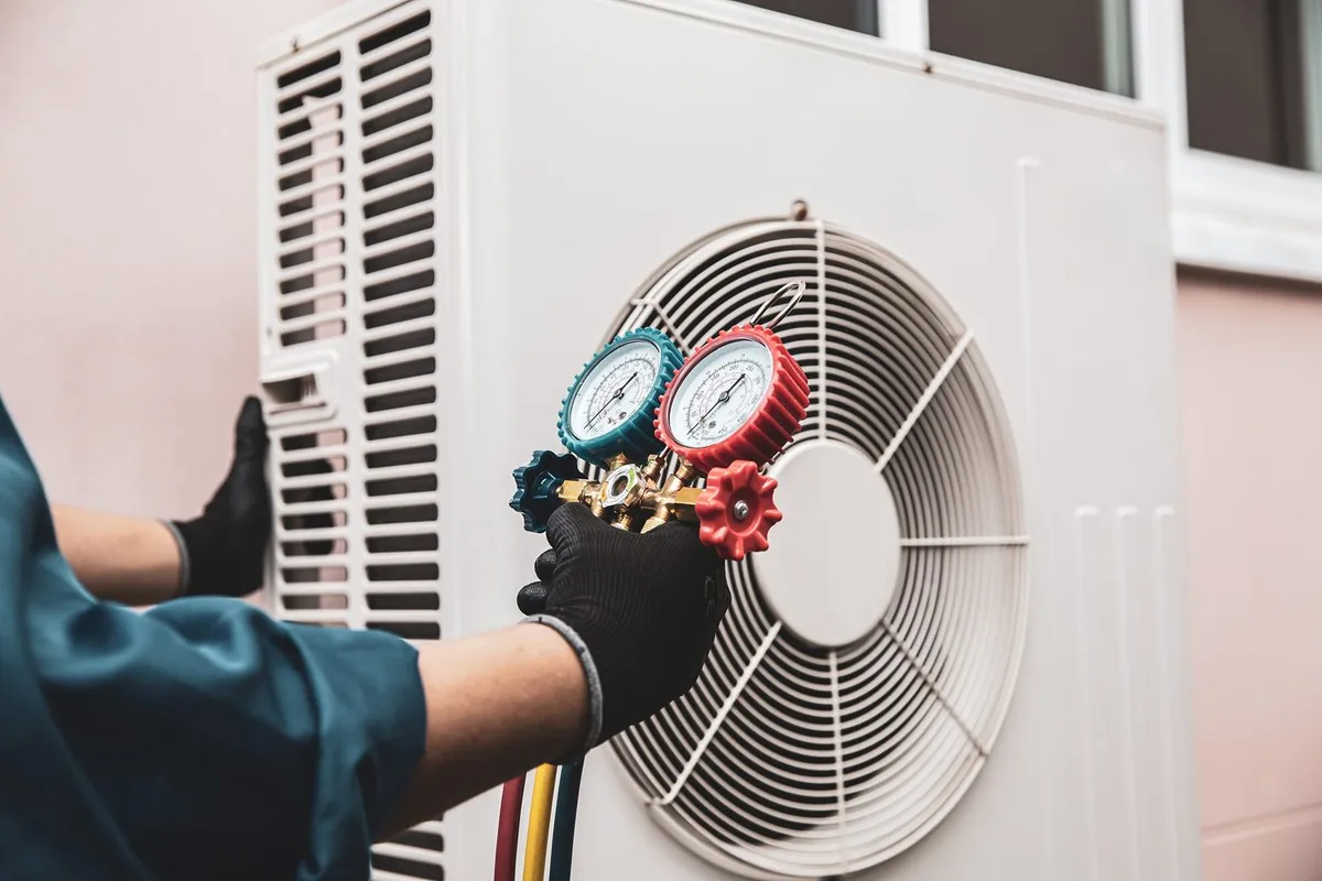 Technician using manifold gauges to service an outdoor air conditioning unit
