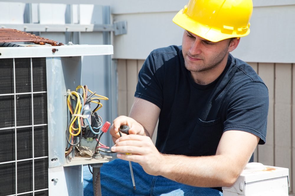 HVAC technician in a hard hat repairing wiring inside an outdoor condenser unit