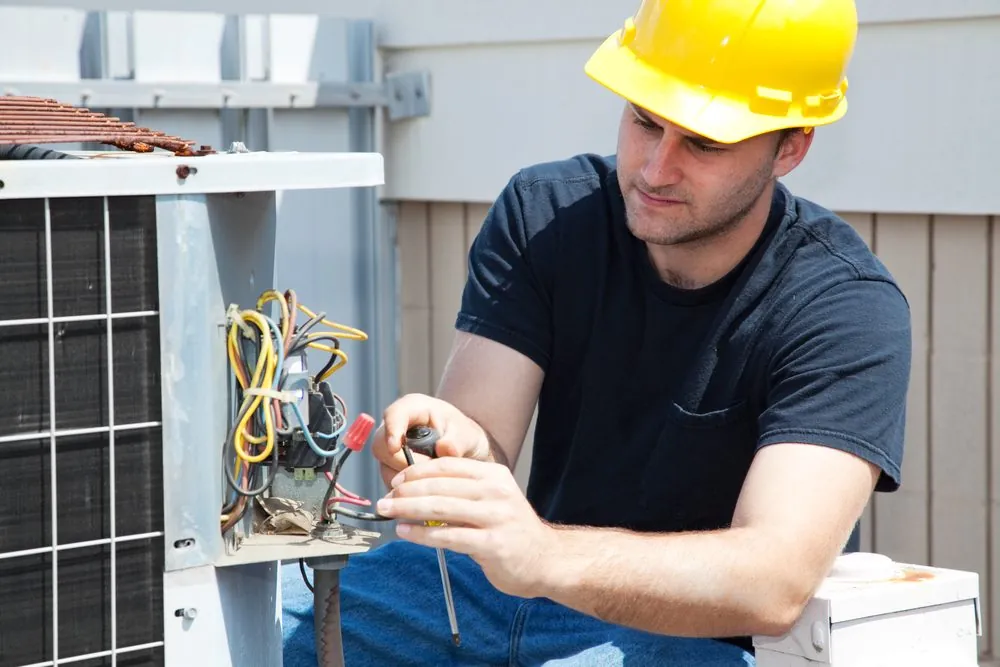 HVAC technician in a hard hat repairing wiring inside an outdoor condenser unit