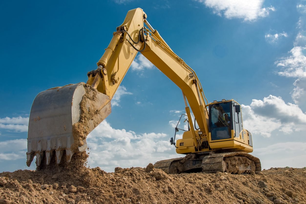 Yellow tracked excavator moving earth on a jobsite against a blue sky