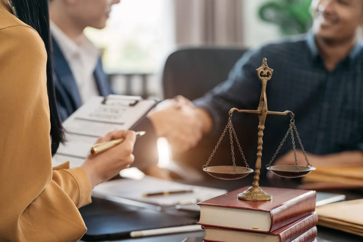 Lawyer shaking hands with a client across a desk with scales of justice and law books