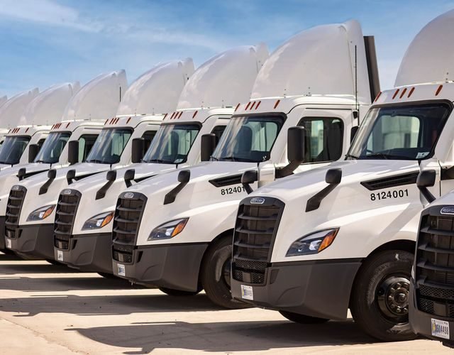 Row of white tractor units lined up in a carrier yard under a clear sky
