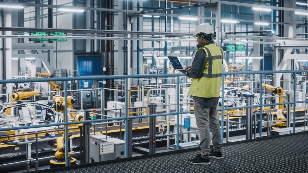 Engineer with a laptop overlooking an automated robotic production line