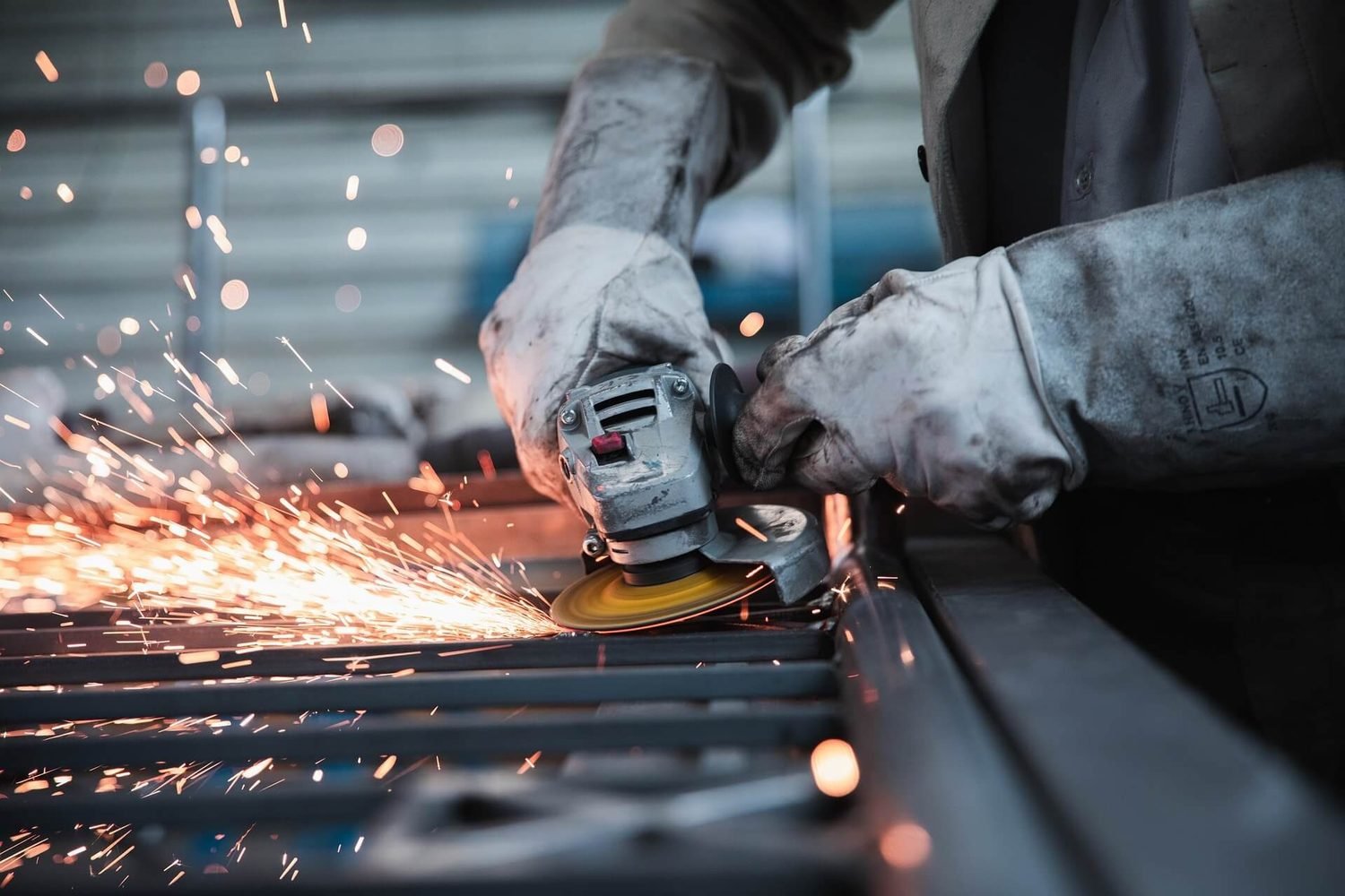 Fabricator using an angle grinder on steel with sparks flying across the bench