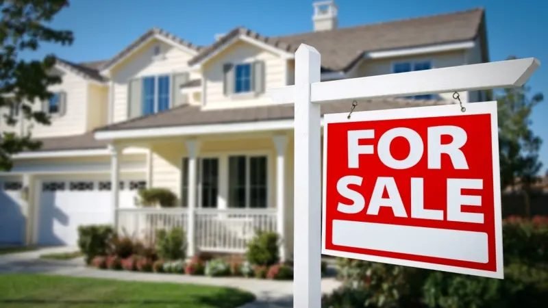 For sale sign in front of a suburban two story home on a sunny day