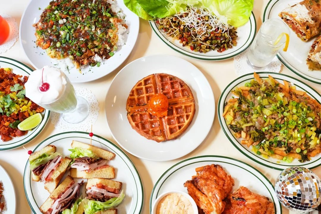 Overhead view of a spread of restaurant dishes, sandwiches, wings, and a milkshake