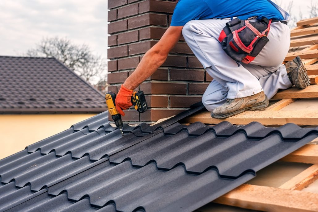 Roofing contractor installing metal roof tiles beside a brick chimney